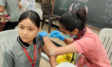 Schoolgirl receiving HPV vaccination at desk